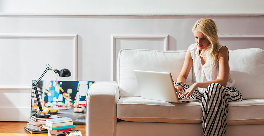 A woman seated on sofa works on laptop